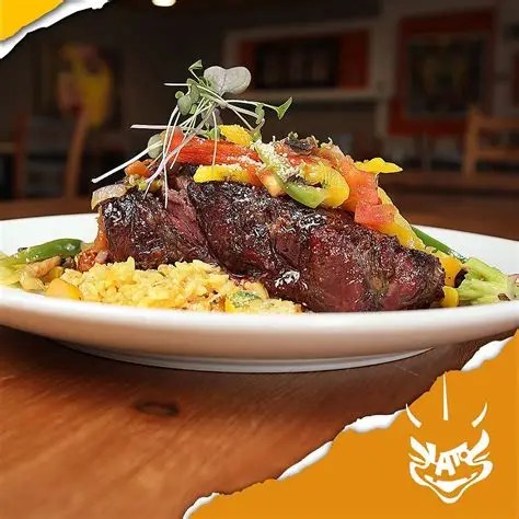 Grilled steak with colorful bell peppers and greens on rice, garnished with sprouts on a white plate.