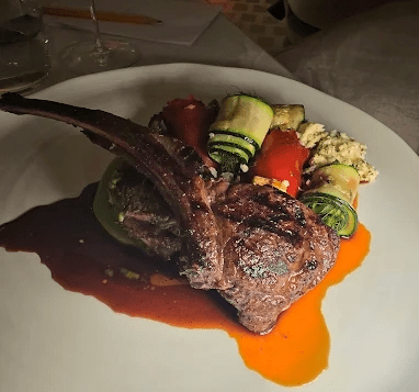 Grilled lamb chop with zucchini rolls and mashed potatoes on a white plate.