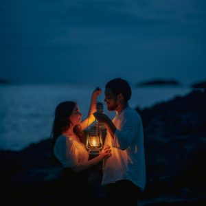 Couple holding a lantern on a beach at dusk.