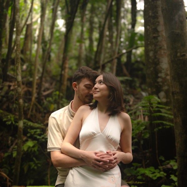 Couple embracing on log in a forest setting.
