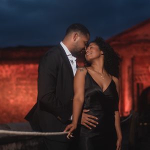 Couple in formal attire embraces under a cloudy evening sky.