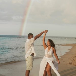 Couple dances on beach with rainbow in the background.