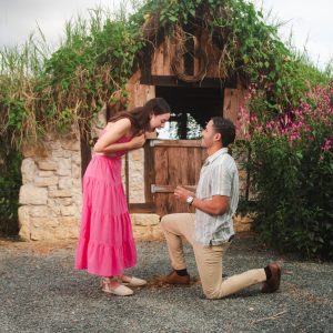 Man proposing to woman in front of rustic hut with flowers.