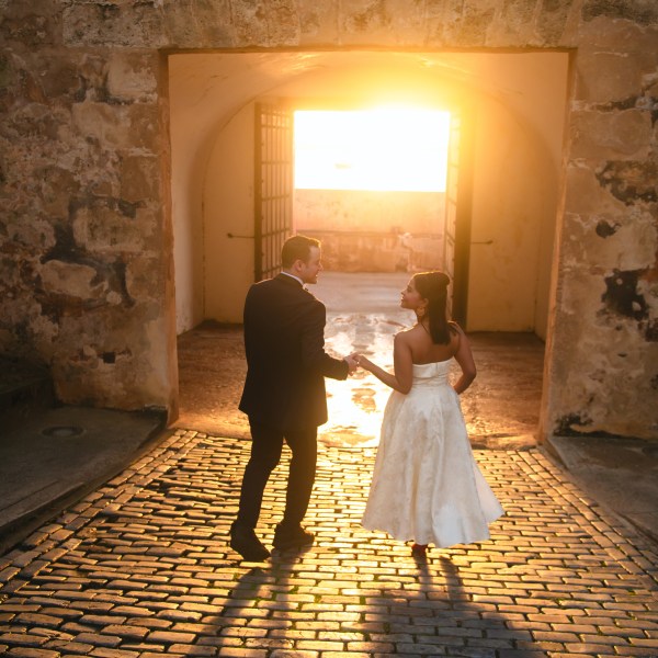 Couple walking hand-in-hand on cobblestone path at sunset.
