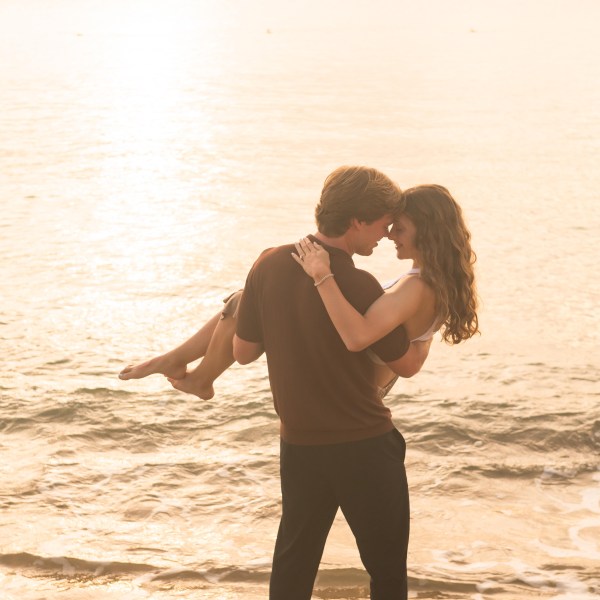 Couple embracing in ocean at sunset, man carrying woman.