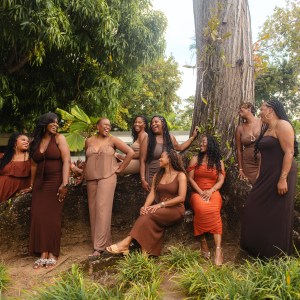 Group of women in earth tones posing by a large tree in a garden setting.